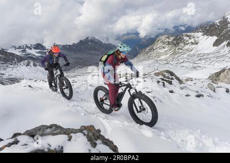 Paar reiten Elektrische fatbikes auf schneebedeckte Berge, Passo di Stelvio, Lombardei, Italien Stockfoto