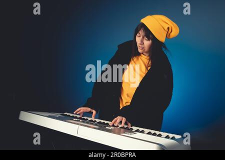 Eine stilvolle und exzentrische weiße Frau mit gelbem Hut und Hemd, die mit Begeisterung auf blauem Hintergrund die Tastatur spielt. Stockfoto