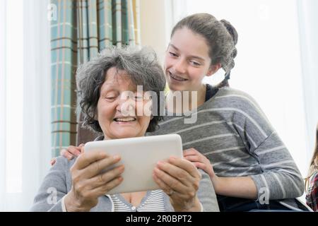 Seniorin mit Enkeltochter, die ein digitales Tablet in einem Heim benutzt Stockfoto