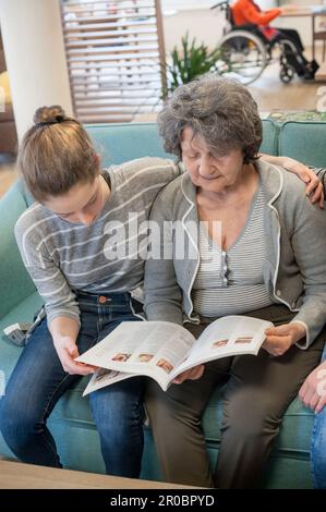 Mädchen lesen Zeitschrift mit Seniorin im Altersheim Stockfoto