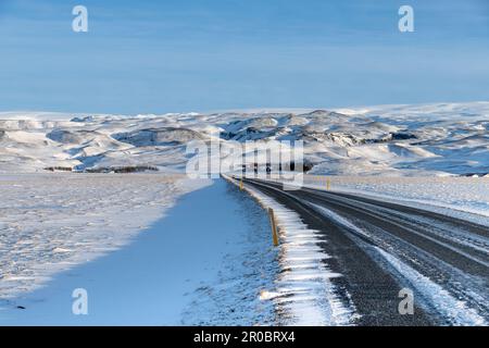 Sehen Sie die Ringstraße 1 im Süden Islands, biegen Sie sich durch eine schneebedeckte Berglandschaft und die Straße, die vor kurzem von Schnee befreit wurde Stockfoto