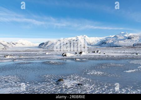 Blick aus niedrigem Winkel über schneebedeckte Landschaft in der Nähe von Svinafell, Island, mit dem Svínafellsjokull und dem Skaftafell-Gletscher im Hintergrund Stockfoto