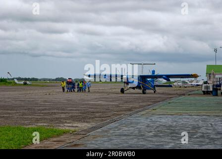 Flughafenangestellte, die Gepäckwagen zum Terminalgebäude am Port-Gentil Airport im westafrikanischen Land Gabun Rollen, um die Regenzeit zu verdunkeln Stockfoto