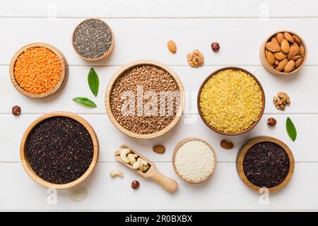 Verschiedene Superfoods in der kleinen Schüssel auf farbigem Hintergrund. Superfood wie Reis, Chia, Quinoa, Linsen, Nüsse, Sesamsamen, Mandeln. Kopierbereich der Draufsicht. Stockfoto