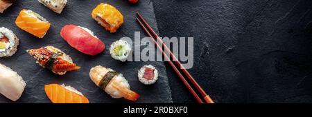 Sushi Overhead Panorama mit Essstäbchen und Kopierbereich. Brötchen, Maki, Nigiri auf schwarzem Hintergrund, japanisches Essen. Lachs, Thunfisch, Aal, Garnelen A. Stockfoto