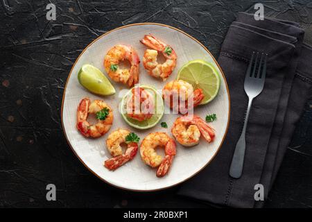 Shrimps, Kopfschuss. Gebratene Garnelen mit Limette auf einem Teller, von oben auf schwarzem Steinhintergrund geschossen Stockfoto