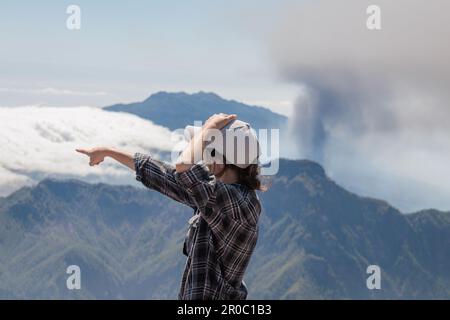 Touristenmädchen zeigt neben dem Vulkanausbruch Cumbre Vieja auf der Insel La Palma, Kanarische Inseln. Vulkan La Palma aus der Vogelperspektive. Stockfoto