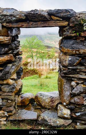 Blick durch ein Fenster in den Überresten des Cwm Ciprwth Copper Mine Gebäudes über dem Cwm Pennant im Snowdonia National Park. Llanfihangel, Gwynedd, Wales, Großbritannien Stockfoto