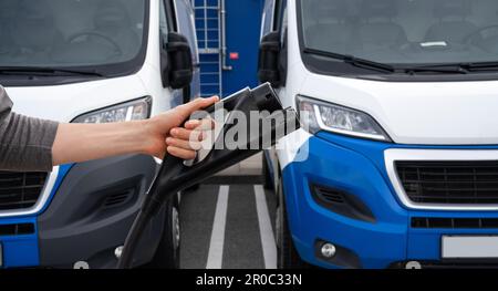 Hand mit Ladestecker für Elektrofahrzeuge auf einem Hintergrund von Elektrotransportern. Hochwertiges Foto Stockfoto