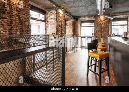 Eine lokale Bar mit hohen Sesseln mit gelben Sitzen, industriellem Parkettboden und kalten Backsteinwänden Stockfoto