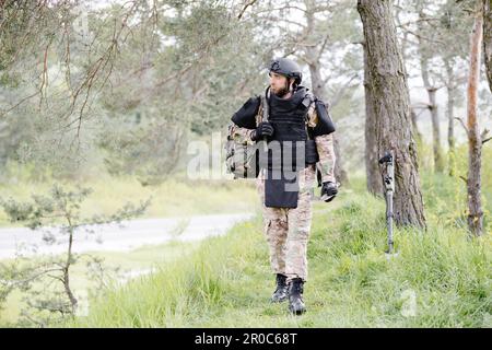 Ein junger Soldat in Uniformen und taktischer Weste arbeitet im Wald und bereitet sich auf die Aktion an einem temporären Waldstützpunkt vor. Ein Mann tut es bei der Minenräumung Stockfoto