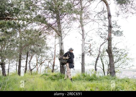 Ein junger Soldat in Uniformen und taktischer Weste arbeitet im Wald und bereitet sich auf die Aktion an einem temporären Waldstützpunkt vor. Ein Mann tut es bei der Minenräumung Stockfoto