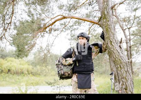 Ein junger Soldat in Uniformen und taktischer Weste arbeitet im Wald und bereitet sich auf die Aktion an einem temporären Waldstützpunkt vor. Ein Mann tut es bei der Minenräumung Stockfoto