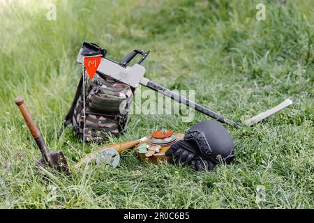 Sprengkörper und ein Metalldetektor liegen auf dem Hintergrund eines Waldmassivs. Ausrüstung für die Minenräumung des Gebiets. Stockfoto