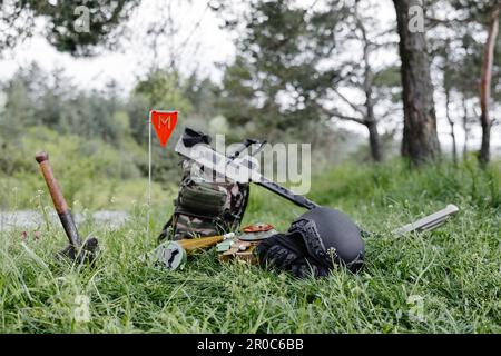 Sprengkörper und ein Metalldetektor liegen auf dem Hintergrund eines Waldmassivs. Ausrüstung für die Minenräumung des Gebiets. Stockfoto