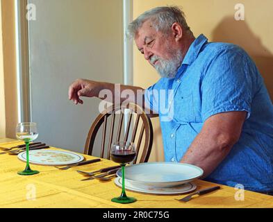 Ein einsamer Seniorenmann, der vor kurzem hintergangen ist. Er sitzt auf seinem eigenen Essen mit seinen Partnern und leerem Platz. Stockfoto