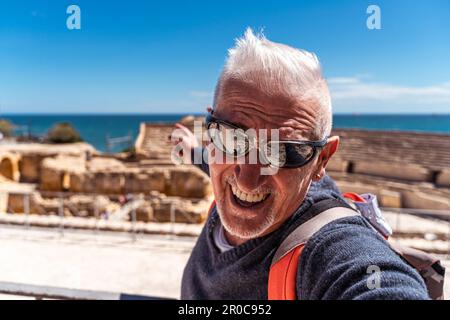 Ein hübscher Mann mittleren Alters, der den archäologischen Komplex tarraco, Tarragona, besucht - glücklicher Tourist, der ein Selfie vor den römischen Ruinen macht - Tourismus und holi Stockfoto