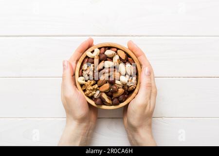 Frauenhände halten eine Holzschüssel mit gemischten Nüssen, Walnuss, Pistazien, Mandeln, Haselnüssen und Cashews. Gesundes Essen und Snack. Vegetarische Snacks dif Stockfoto
