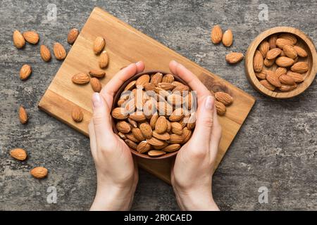 Frauenhände halten eine Holzschüssel mit Mandelnüssen. Gesundes Essen und Snack. Vegetarische Snacks mit verschiedenen Nüssen. Stockfoto