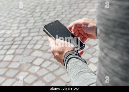 Ein Mann mit einem Smartphone in der Hand sitzt mitten in der Stadt bei Tageslicht Stockfoto