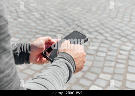 Ein Mann mit einem Smartphone in der Hand sitzt mitten in der Stadt bei Tageslicht Stockfoto
