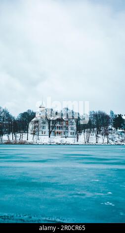 Eine Winterszene mit einem majestätischen weißen Gebäude über einem ruhigen See, gefroren durch die kalten Wintertemperaturen Stockfoto