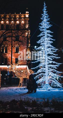 Eine festliche Winterszene mit einer Familie, die im Winter bei Nacht vor dem hellen Weihnachtsbaum Spaß hat Stockfoto