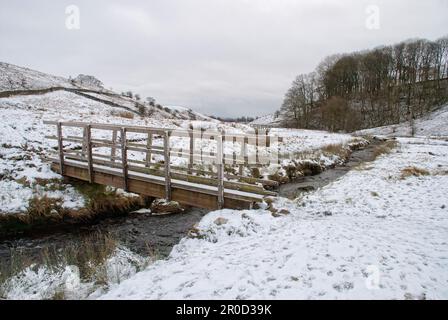 Schneeszene mit Holzbrücke über dem Long Preston Beck im Yorkshire Dales National Park. Stockfoto