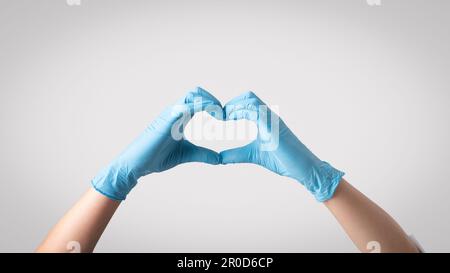 Betonung von Mitgefühl im Gesundheitswesen. Eine Ärztin mit Schutzhandschuhen, die mit ihren Händen eine Herzform bildet Stockfoto