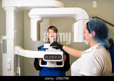 Der Röntgentechniker macht einen CT-Scan der Kiefer-Patientin. Frau mit kreisförmigem Kieferschnappschuss in der modernen Zahnheilkunde. Computertomographische 3D-Tomographie der Zähne. Pano Stockfoto