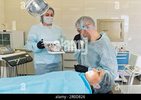 Die Krankenschwester zeigt dem Chirurgen das Röntgenbild, bevor sie den Backenzahn von der Patientin entfernt Stockfoto