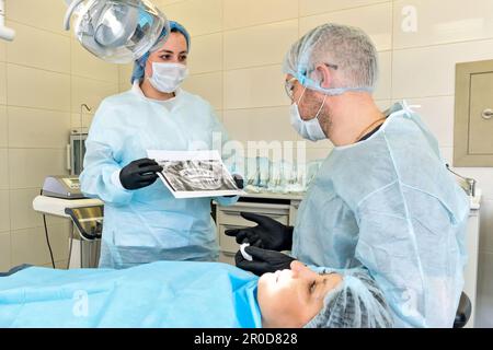 Die Krankenschwester zeigt dem Chirurgen das Röntgenbild, bevor sie den Backenzahn von der Patientin entfernt Stockfoto