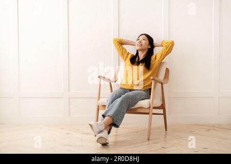 Entspannte junge asiatische Frau, die sich zu Hause in einem Sessel entspannt Stockfoto