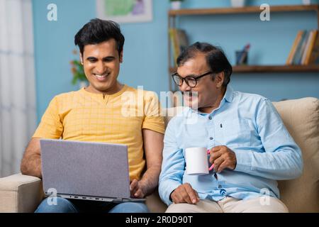 Glücklicher indischer Erwachsenensohn, der seinem Seniorenvater sein Notebook zeigt, indem er zu Hause diskuziert - Konzept von Wochenendferien, Beziehung und Entspannung. Stockfoto