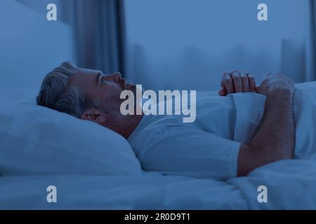 Schlafloser Mann mittleren Alters, der nachts im Bett liegt Stockfoto