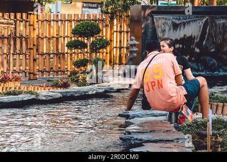 KANCHANABURI -THAILAND, 30. MÄRZ 2023 : Unbekannte Touristen kommen zu Besuch und füttern Koi oder schicke Karpfen in einem kleinen Teich mit schönem Garten Stockfoto