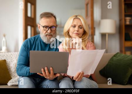 Reife Ehepartner, Die Papierrechnungen Prüfen Und Zu Hause Ein Notebook Verwenden Stockfoto