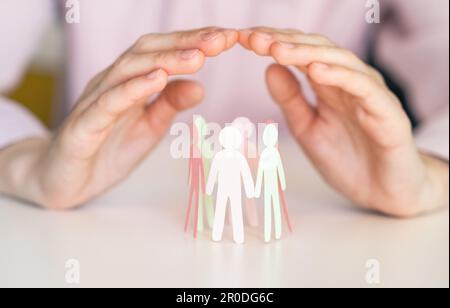 Frau, die Papiermenschen auf einem hellweißen Tisch beschützt, Nahaufnahme. Stockfoto