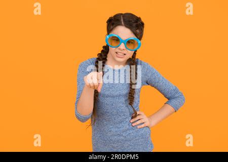 Sonnenbrillen sind gesundheitliche Notwendigkeit. Unzufrieden Kind gelben Hintergrund. Get Party started. Kid Zeigefinger. Porträt des Mädchens in lustigen Brillen. Jung Stockfoto