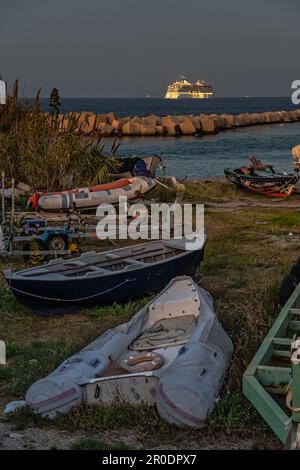 Das Kreuzfahrtschiff, beleuchtet durch das warme Licht des Sonnenuntergangs, überquert die Straße von Messina. Im Vordergrund zogen kleine Boote an Land. Kalabrien Stockfoto