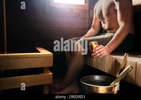 Sauna und Bier. Mann im Dampfbad entspannt und trinkt etwas. Traditionelles finnisches Wellnesszentrum aus dunklem Holz oder im Wellness-Hotel in Finnland. Stockfoto