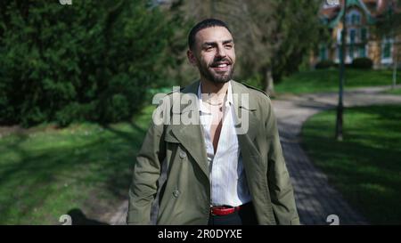 Ein freudiger junger arabischer Mann, der einen gemütlichen Spaziergang durch einen sonnigen Park macht und sich in der Wärme der Sonne und der Schönheit der Natur sonnt Stockfoto