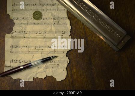 Ein antiker Tintenstift liegt auf einem Blatt Papier, das mit Noten bedeckt ist und eine zeitlose Melodie erzeugt Stockfoto