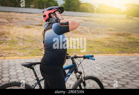 Sportlicher Radfahrer, der beim Radfahren Nackenschmerzen hat. Männlicher Radfahrer mit Nackenschmerzen im Freien Stockfoto