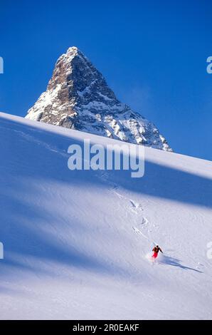 Junger Mann, der im Tiefpulverschnee vor dem Matterhorn, Grisons, Schweiz, Ski fährt Stockfoto