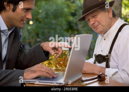 Junger Geschäftsmann und älterer bayerischer Mann im Biergarten, München, Bayern Stockfoto