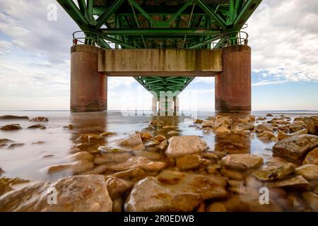 Eine Nahaufnahme einer grünen Metallbrücke, die einen breiten Fluss überspannt und zwei Ufer verbindet Stockfoto