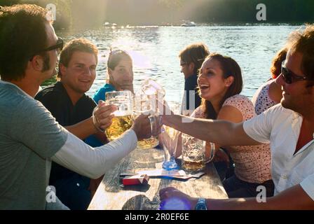 Junge Leute sitzen und toasten im Biergarten, Seehaus, Englischen Garten, München Stockfoto