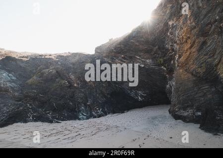 Der Strand ist geschützt unter einem hohen Felsen, in den die ersten Sonnenstrahlen in der Region Odemira im Westen Portugals fließen. Sie wandern am Fisch entlang Stockfoto