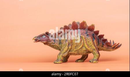 Ein Spielzeugdinosaurier der Art Stegosaurus auf orangefarbenem Hintergrund Stockfoto